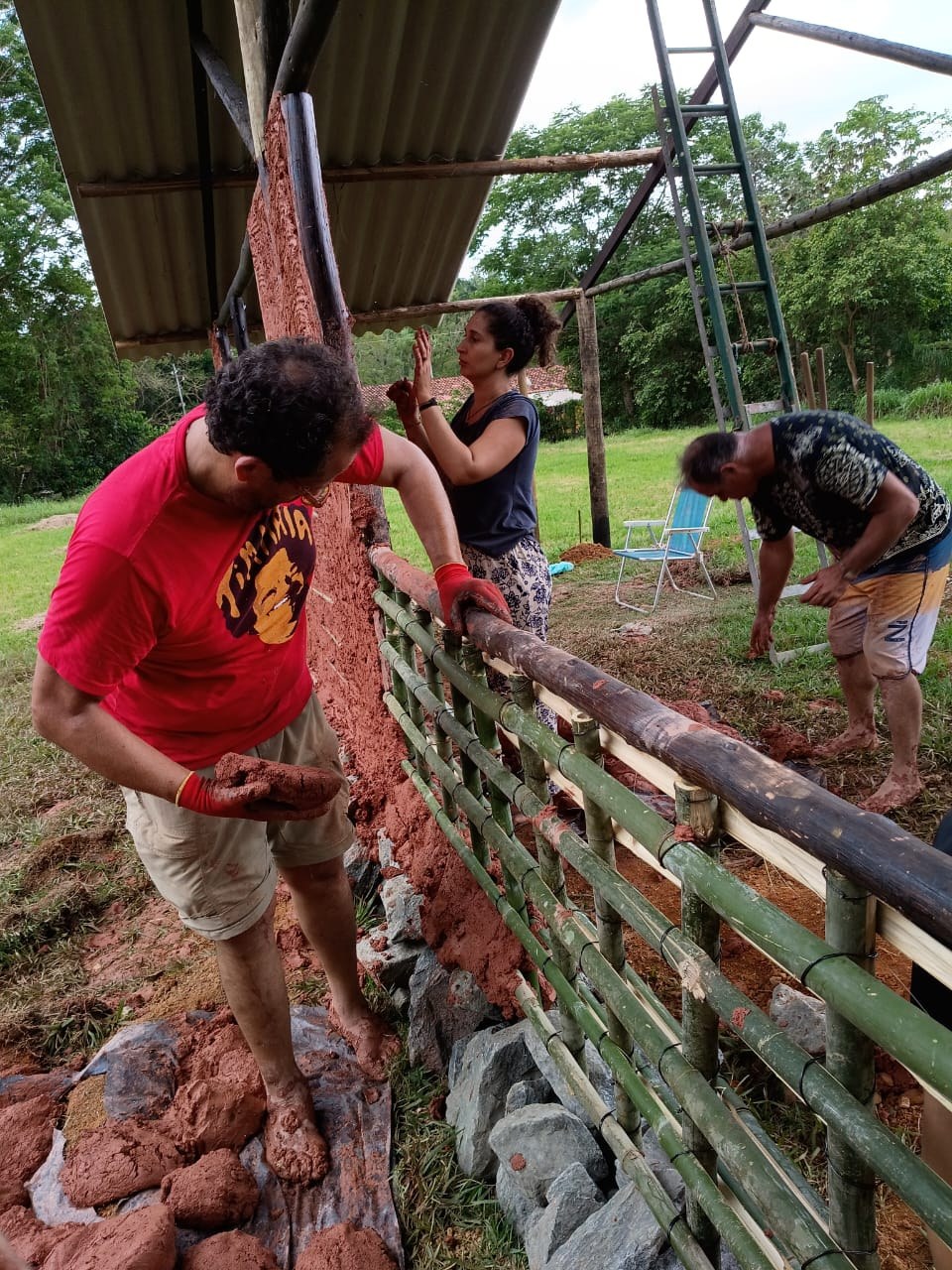 Participantes aplicando barro na estrutura de bambu